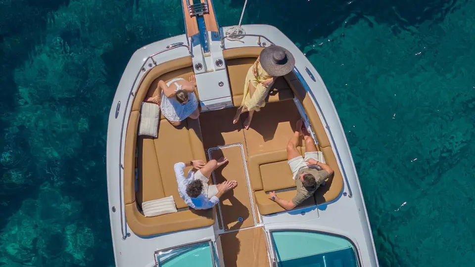 Jeanneau TH33: overhead view of the bow lounge with tan U-shaped seating and four people relaxing