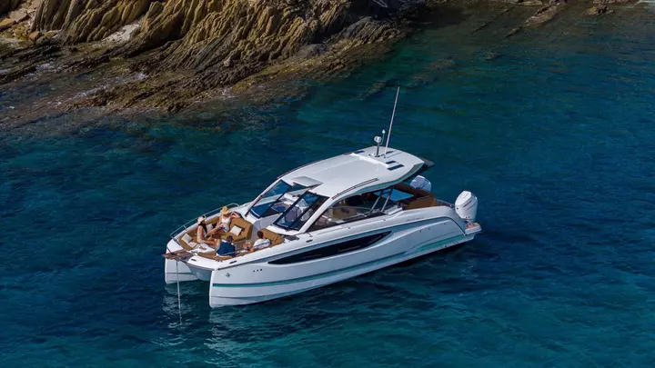 Jeanneau TH38: aerial view at anchor showing hardtop, foredeck lounge with guests and twin outboard engines