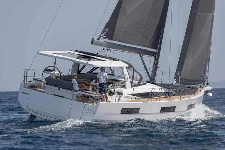 Jeanneau Yachts 60: white-hulled yacht under sail from the stern quarter, two people in the cockpit beneath a hardtop bimini