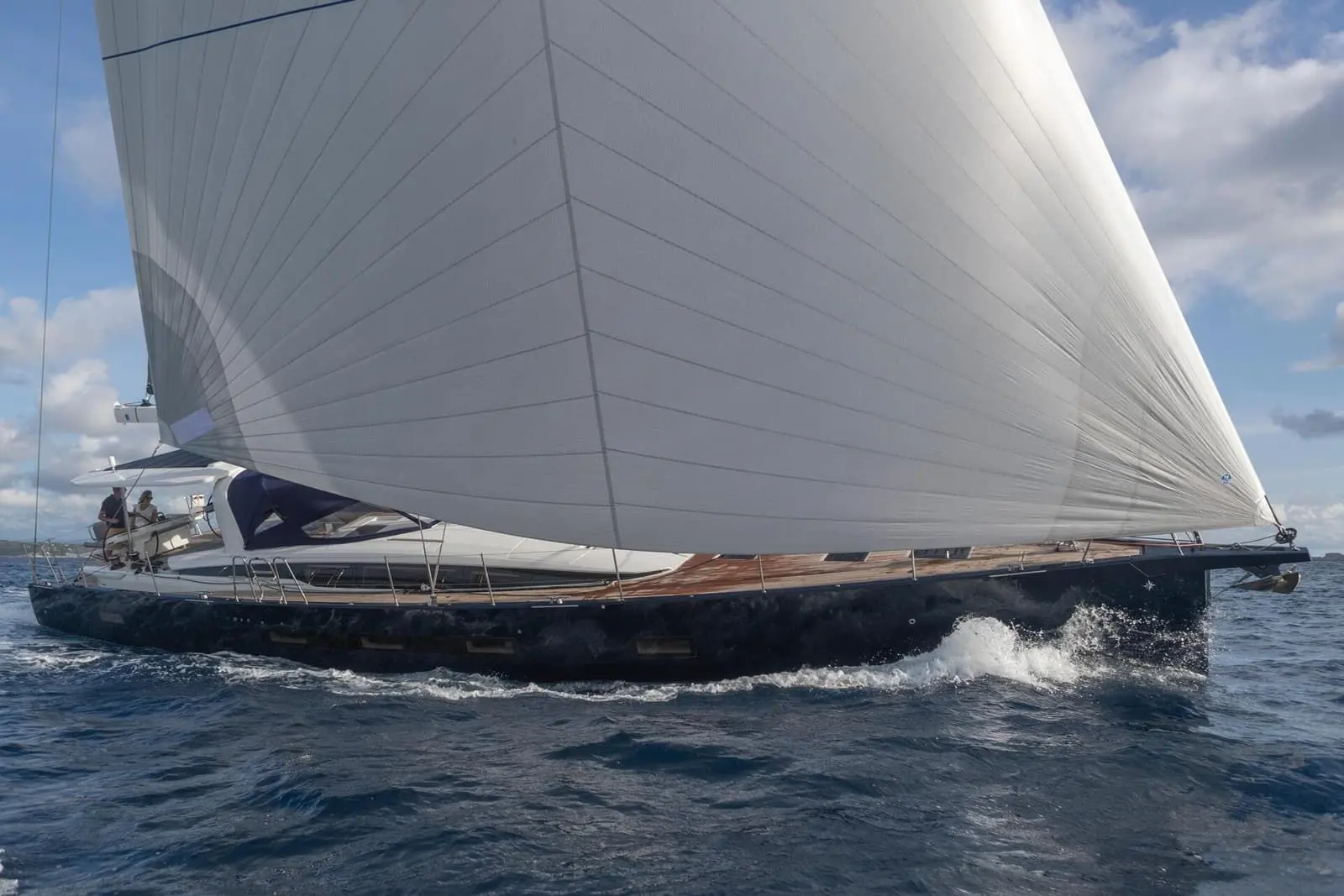 Jeanneau Yachts 65: dark-hulled yacht under sail with a large white headsail, crew in the cockpit