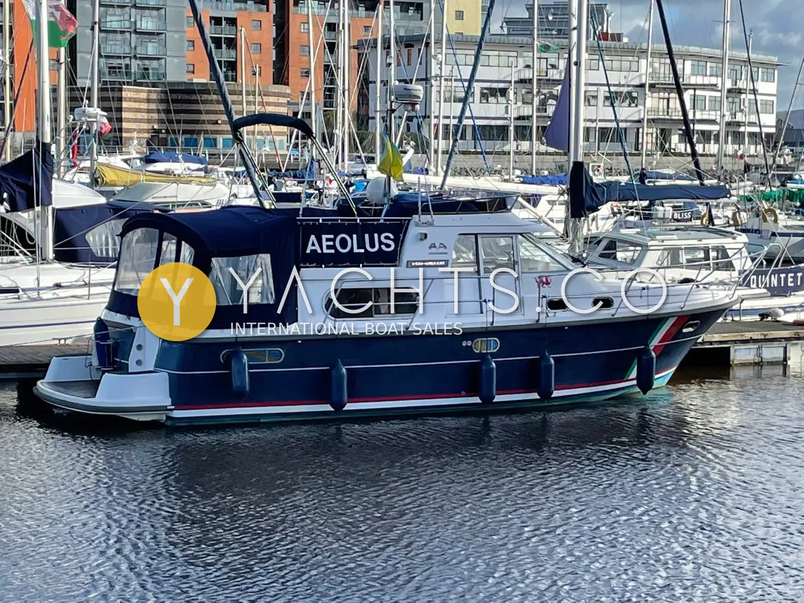 Nimbus 380 Commander: navy and white hull with blue canopy moored in a marina beside waterfront buildings