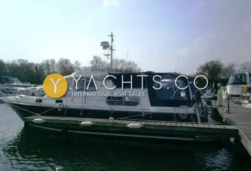 Nimbus 380 Commander: blue-hulled flybridge cruiser moored alongside a pontoon with canopy fitted, trees behind