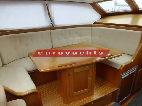 Nordship 380 DS: cream upholstered saloon seating around fixed teak dining table under large windows