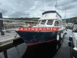 Northshore Yachts Sabreline 395 Trawler: navy-hulled trawler with fenders out, berthed in a marina with green hills behind