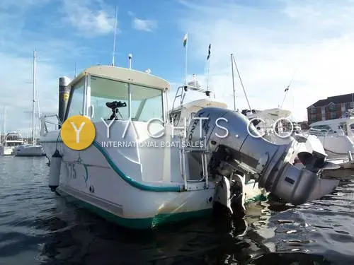 Ocqueteau 575: stern quarter view in a marina showing the outboard tilted up and the white pilothouse