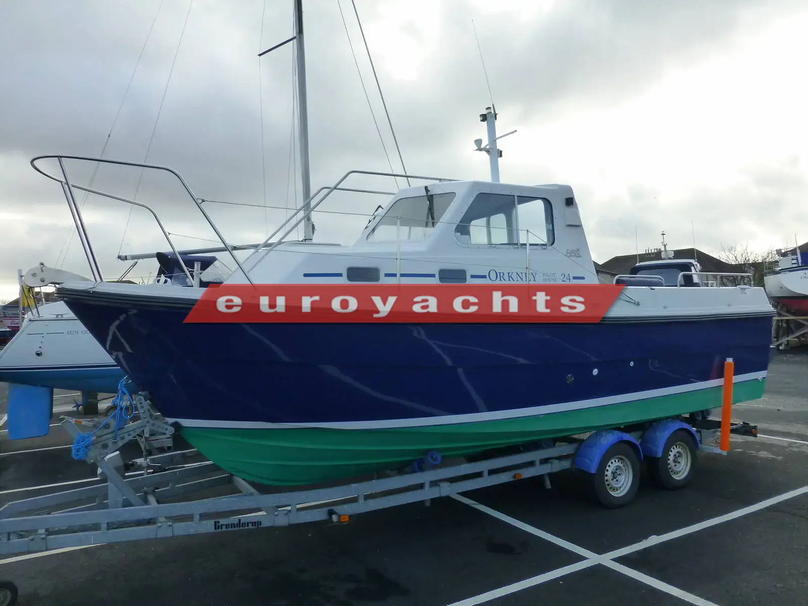 Orkney Boats Pilothouse 24: blue-hulled pilothouse boat with green antifouling on a twin axle trailer in a boatyard