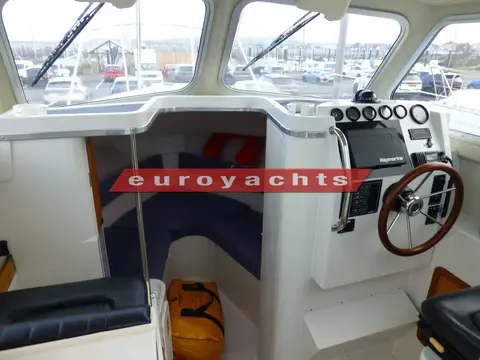 Orkney Boats Pilothouse 24: wheelhouse interior with helm and wheel to starboard and steps down to the blue forward cabin