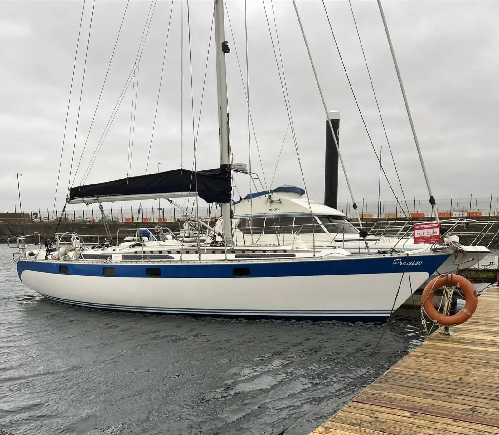 Oyster 435: blue-striped white hull afloat alongside a pontoon, sail cover on boom and lifebuoy on rail