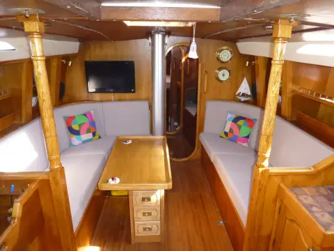 Oyster 435: saloon looking forward, settees either side of a central wooden table, TV on bulkhead