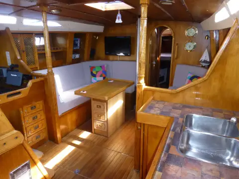 Oyster 435: saloon with L-shaped settee, wooden table, wood floor and galley sink in the foreground