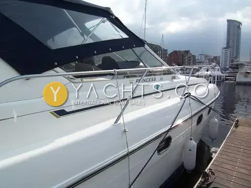Princess 366: starboard side with polished white hull, blue stripe and canopy, moored in a marina beside a tower block