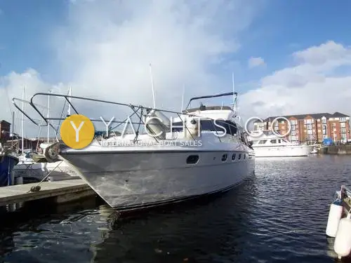 Princess 480 Flybridge: bow three-quarter view of the white flybridge cruiser moored at a marina pontoon beside apartment blocks