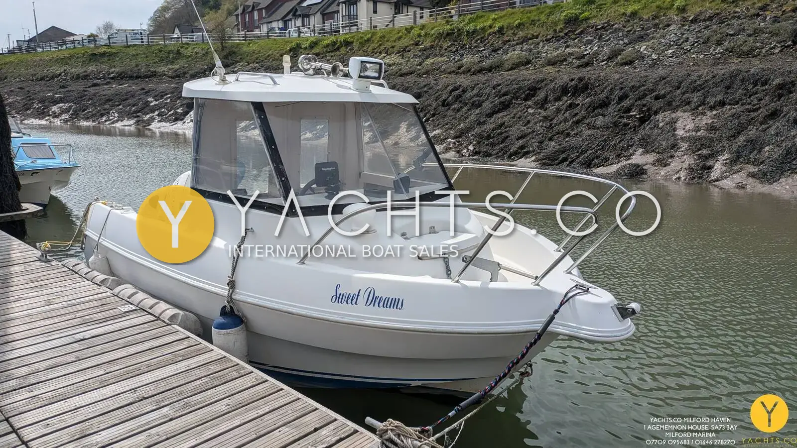 Quicksilver 500 Pilothouse: white pilothouse hull moored alongside a pontoon, bow and side windows visible, houses behind
