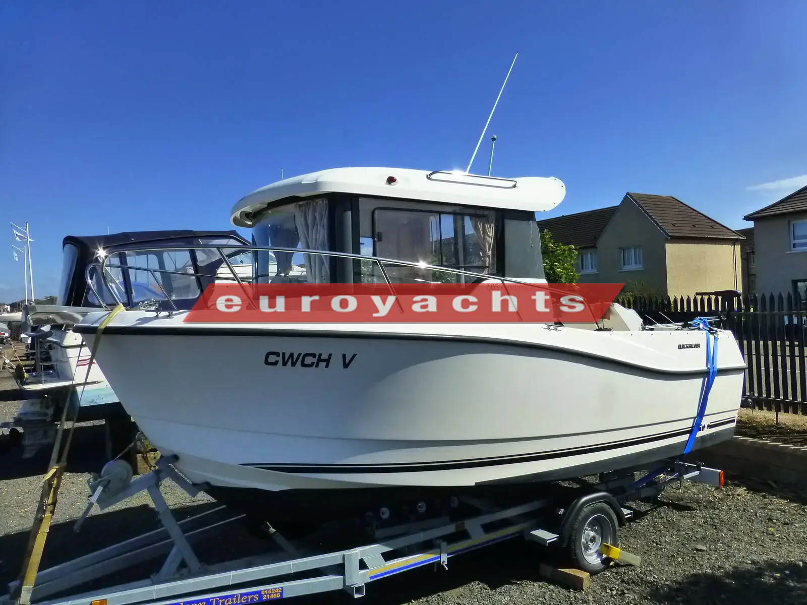 Quicksilver 605 Pilothouse: white hull and pilothouse on a galvanised road trailer, parked ashore beside houses