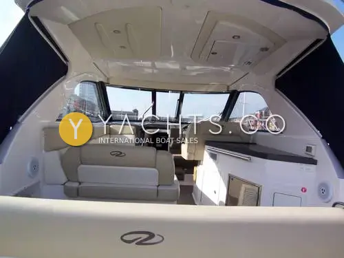Regal 35 Sports Cruiser: cockpit looking forward under the hardtop, cream seating, wet bar and wraparound windscreen