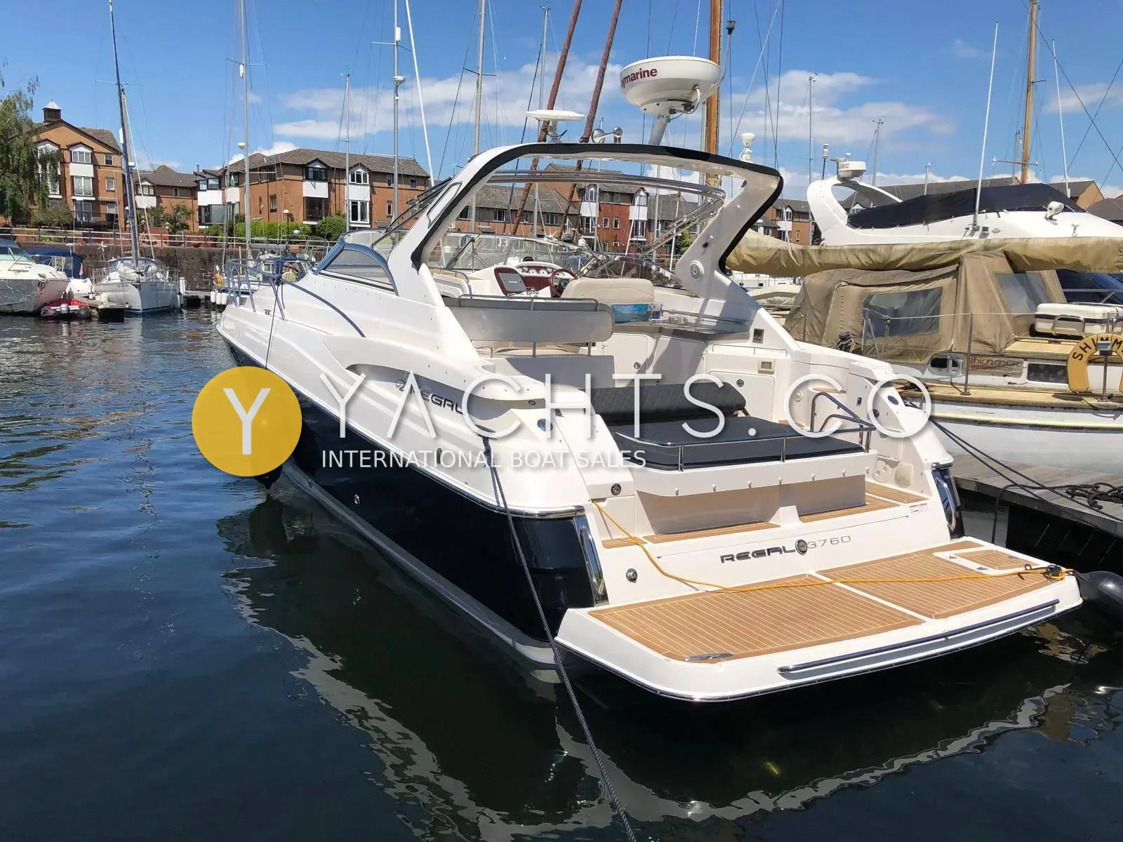 Regal 3760: white sports cruiser with dark hull band moored stern-to in a marina, teak bathing platform