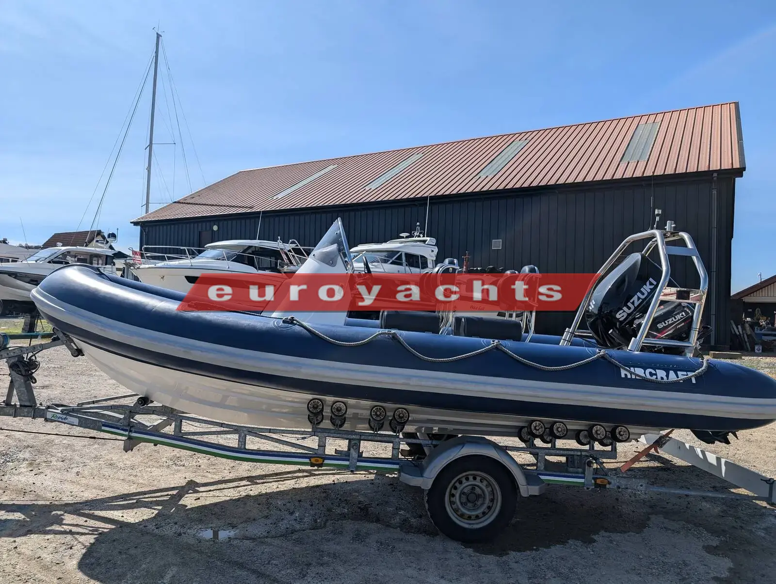 Ribcraft 585: navy and white RIB on a roller trailer beside a dark shed, A-frame at the stern
