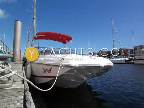 Rinker 210 MTX: bow quarter view of the white hull with red bimini, moored alongside a pontoon in a marina