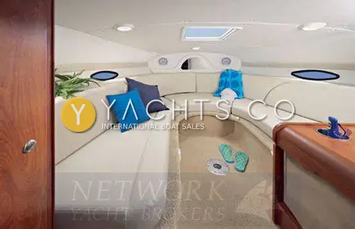 Rinker 230: cabin with cream U-shaped seating, blue cushions, overhead hatch and portholes, brochure-style image