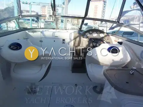 Rinker 230: cockpit under canopy with two white bucket seats, helm dash and wet bar sink