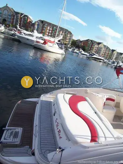 Rinker 232: stern sunpad with red detail and teak-effect bathing platform, marina flats behind