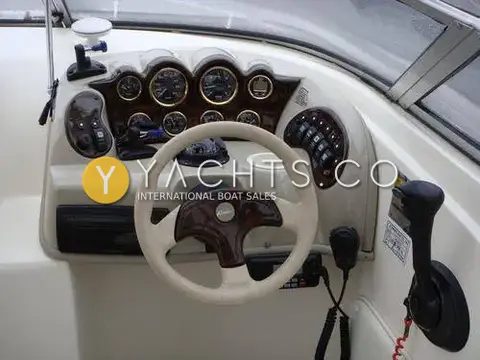 Rinker 232: helm dash with woodgrain gauge panel, cream wheel, VHF handset and throttle lever