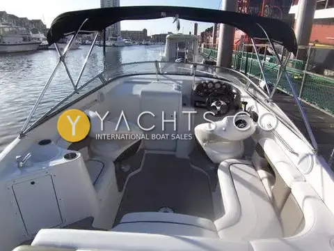 Rinker 232: open cockpit with cream seating, grey carpet and helm under black Bimini, marina behind