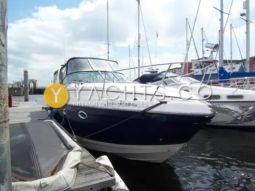 Rinker 270 Fiesta Vee: bow quarter view of the navy blue hull with name on topsides, moored at a marina pontoon