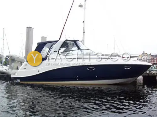 Rinker 280 Express Cruiser: starboard side of the navy and white hull afloat in a marina, with blue camper canopy fitted