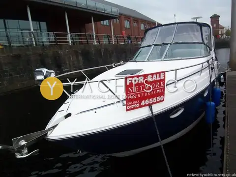 Rinker 280 Express Cruiser: bow and starboard side moored in a dock beside brick buildings, with a for sale board