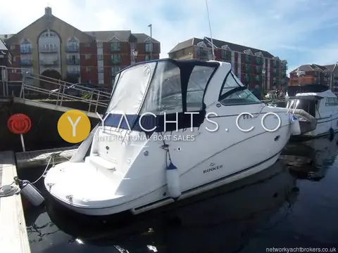 Rinker 330: port quarter view afloat in a marina with brick apartment buildings behind