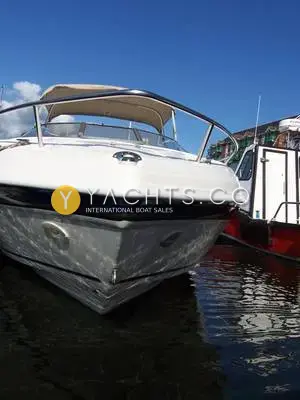 Rinker 232: low bow view of the white hull with blue stripe, moored beside a red boat