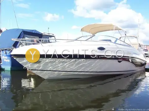 Rinker 232: starboard side profile afloat in a marina, white hull with dark stripe and bimini up