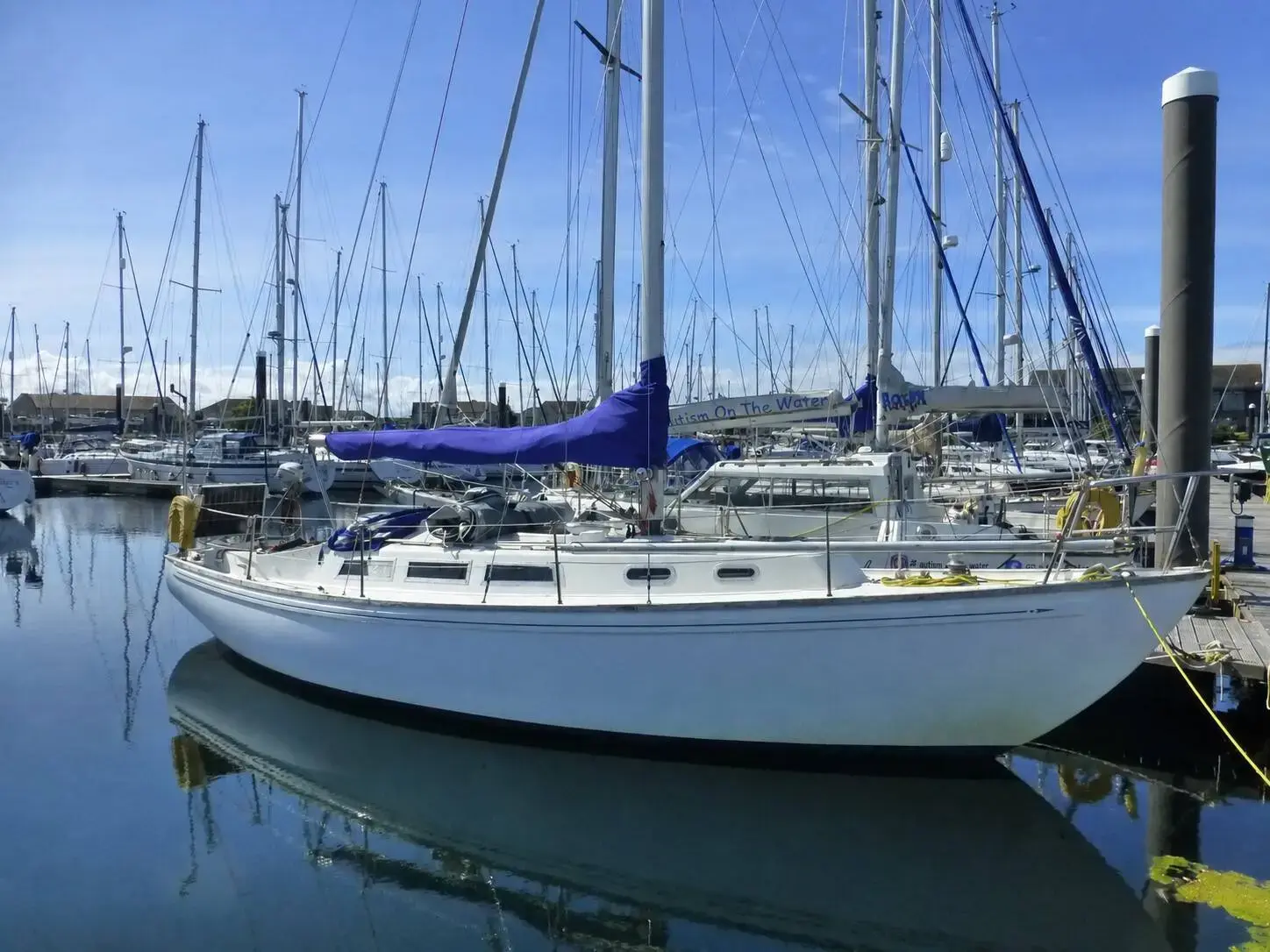 Rival 36: white hull afloat in a marina berth, blue mainsail cover on the boom
