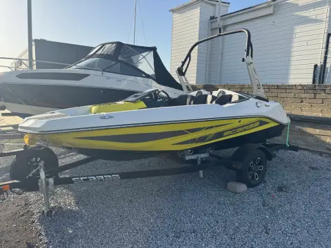 Scarab 165: port side of hull with yellow race graphics and wakeboard tower, sitting on road trailer