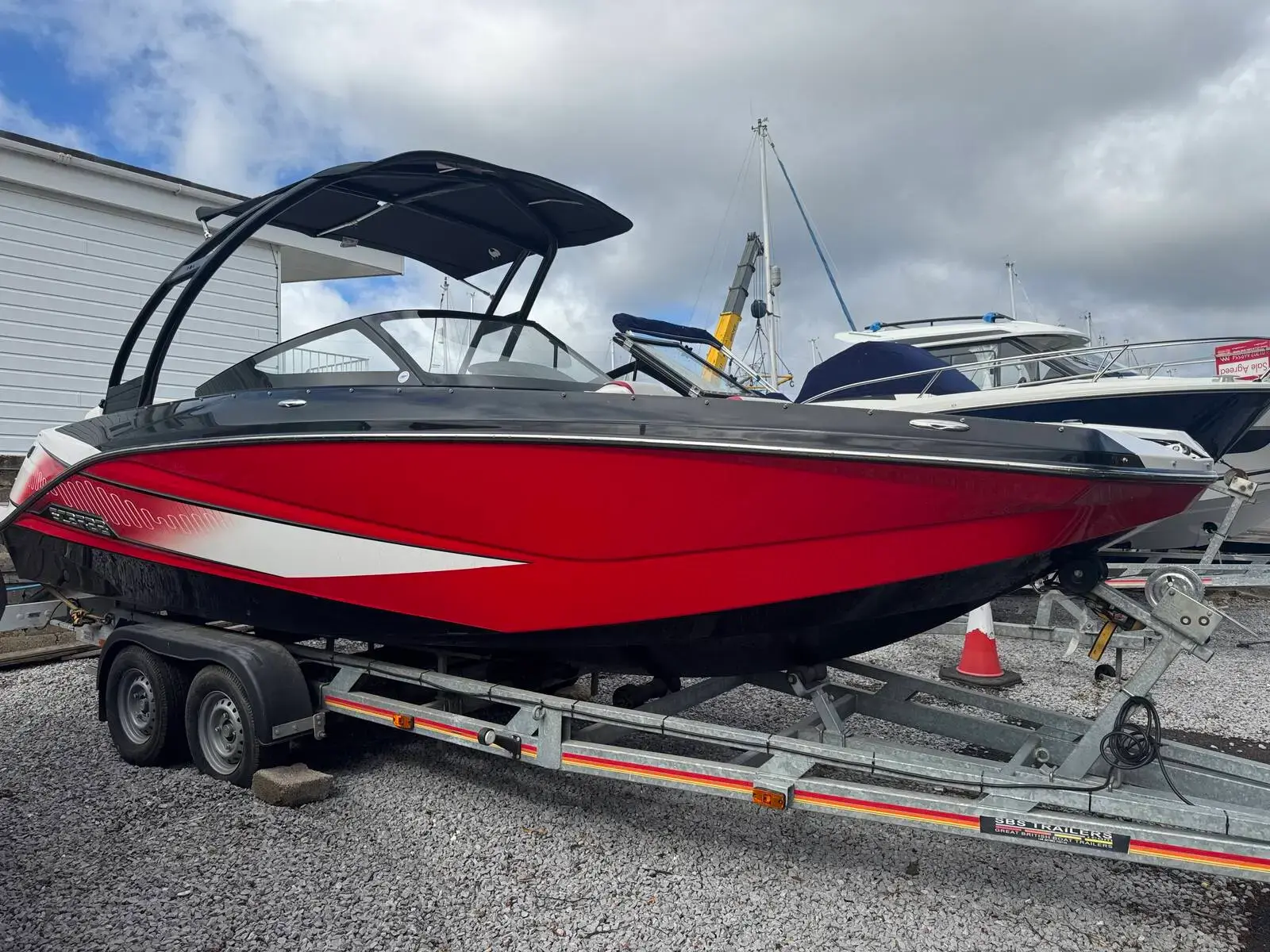 Scarab 215: metallic red and black hull with wakeboard tower and bimini, sitting on a twin axle trailer