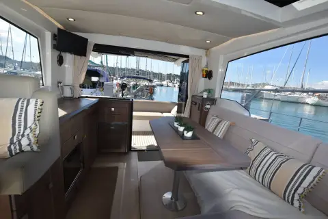 Sealine International C330: saloon with cream sofa, wooden table and large side windows overlooking the marina