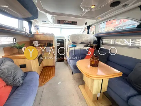 Sealine International F33: saloon with blue upholstered seating, wooden table and light-wood galley to port