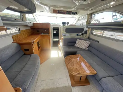 Sealine International F33: saloon with grey upholstered seating, burr wood table and galley looking aft