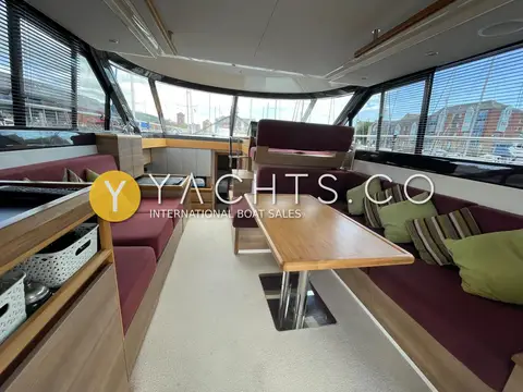 Sealine International F42: saloon with plum seating either side, walnut dining table and marina view through windows