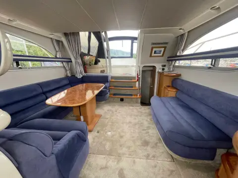 Sealine International F43: saloon with blue upholstered seating, burr walnut table and steps leading aft
