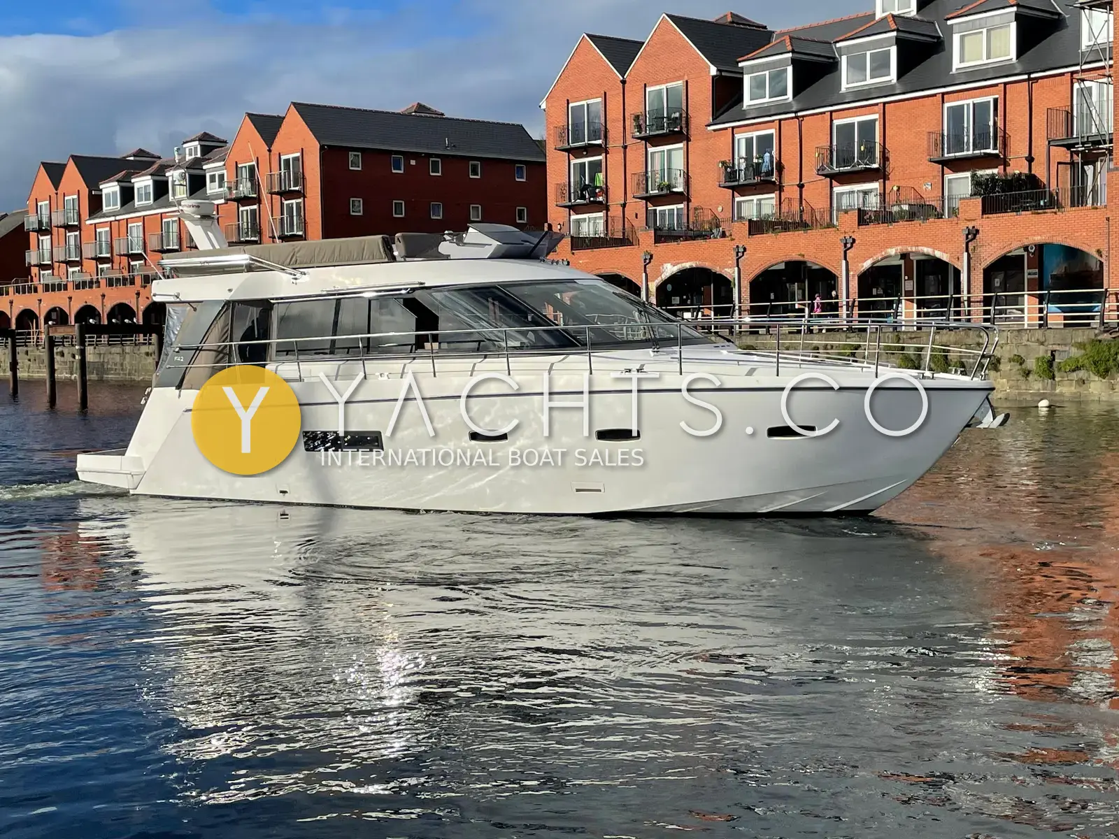 Sealine International F44: white flybridge hull under way in a marina beside red-brick waterfront apartments