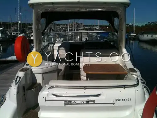 Sealine International Sealine S28 Reduced: stern view of cockpit with white seating, wooden table and wet bar, moored in a marina