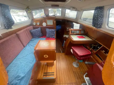 Sovereign 32 Deck Saloon: deck saloon with raised blue-cushioned seating to port and chart table helm to starboard