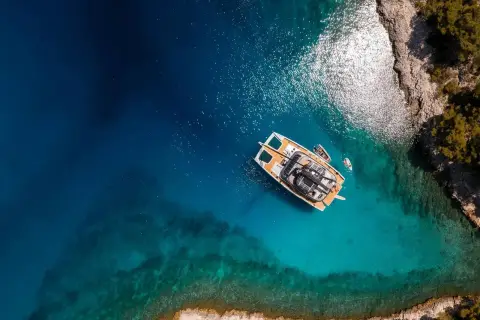 Sunreef Eco 70: aerial view from above of the catamaran anchored over turquoise water beside a rocky shore