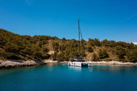 Sunreef Eco 70: catamaran anchored in a quiet cove beneath wooded hillsides