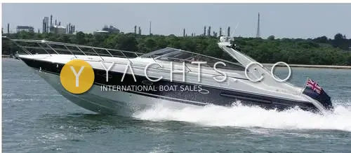 Sunseeker Camargue 47: oxford blue hull underway at speed with red ensign flying, industrial shoreline behind