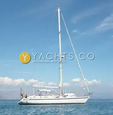 Taswell 49CC: yacht at anchor in calm blue water with mountains behind, sails furled and bimini frame up