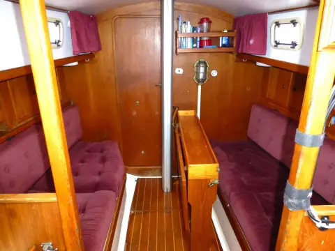 Victoria 30: saloon looking forward with burgundy settees, folded table and door to forward cabin