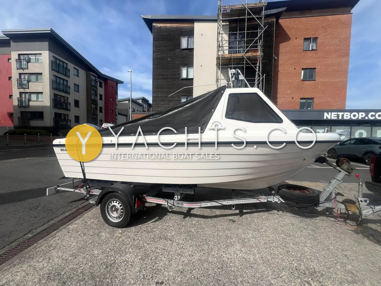 Warrior 165: white hull with dark cockpit cover on a road trailer, parked beside flats